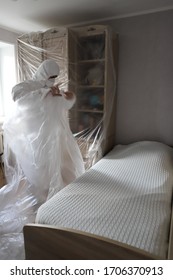 Man In A Protective Medical Suit, Mask And Glasses Seals With Film Furniture, Insanity, Protection From And Repair Dust