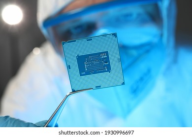 Man in protective suit and glasses holding computer microchip with tweezers closeup. Repair of computer equipment concept