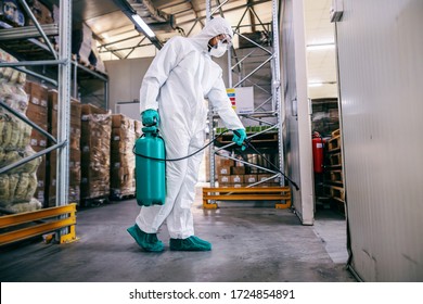 Man In Protective Suit And Mask Disinfecting Warehouse Full Of Food Products From Corona Virus / Covid-19.