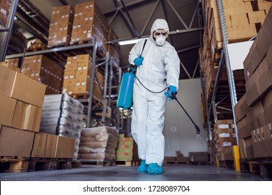 Man In Protective Suit And Mask Disinfecting Warehouse Full Of Food Products From Corona Virus / Covid-19.