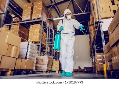 Man In Protective Suit And Mask Disinfecting Warehouse Full Of Food Products From Corona Virus / Covid-19.