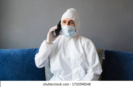 Man in protective suit, medical mask and rubber gloves sits at home and speaking with a friends or business partners on a sofa during quarantine. Man at remote work in a pandemic covid. - Shutterstock ID 1710398548