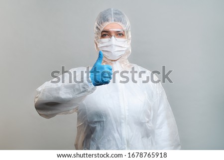 Man in protective suit, medical mask, safety glasses with raised finger up isolated in studio
