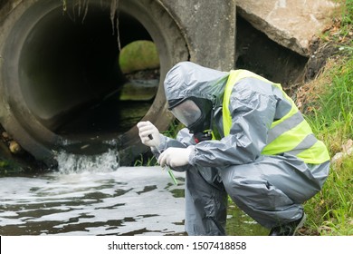 A Man In A Protective Suit Takes A Sample Of Water From The River After The Release Of Chemical Waste