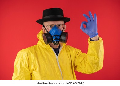 A man in a protective yellow suit and chemical mask, glasses and a black hat shows the sign OK. The image of Walter White, Heisenberg. Concept Breaking Bad. Underground Chemist.