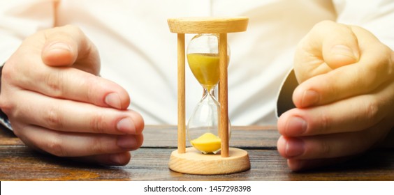 Man Protects The Hourglass. Concept Of Saving Time And Money. Time Management. Planning Work. Reduced Cost And Bureaucratic Burden. Saving Productivity. Extension Of Life. Debt / Tax Holidays