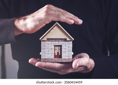 A man protects a small house with his hands. The concept of home protection