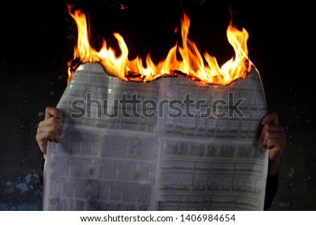 Man protesting fake media news, burning newspaper, dark mode.Burning newspapers in the hand of a man.Against the dark background