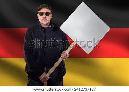Man protesting near German flag. Participant in street demonstration with poster. Protester holds blank banner. Street protest in Germany. Worker takes part in strike. German protester.
