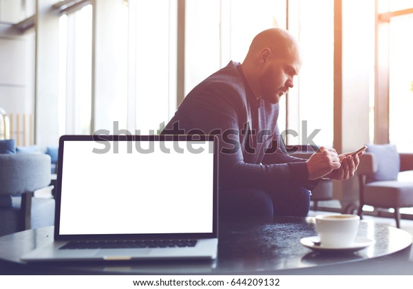 Man proud CEO is ordering o-nline via cell\
telephone car for business trip, while is sitting in co-working\
cafe near table with open laptop computer with empty copy space\
screen for your advertising