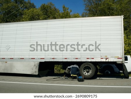 a man pulled over on the side of the highway with a huge semi truck tries to repair an issue with a tire on a sunny day on the road