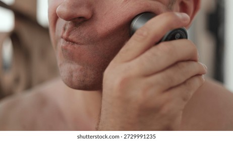Man pulling cheek to shave precise areas, closeup of hand gripping trimmer and skin stretching for even cut, concentrated expression and small controlled movements, intimate technical grooming moment