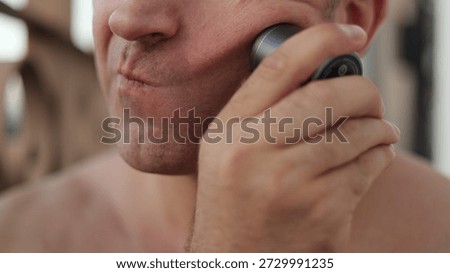 Man pulling cheek to shave precise areas, closeup of hand gripping trimmer and skin stretching for even cut, concentrated expression and small controlled movements, intimate technical grooming moment