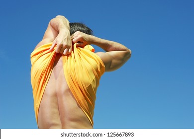 Man Pulling Up His Shirt At The Back, Showing His Back With Blue Sky At The Background