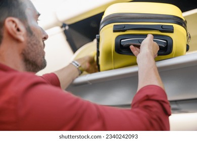 Man pulling out hand luggage from compartment while traveling by plane. Vacation, transportation concept