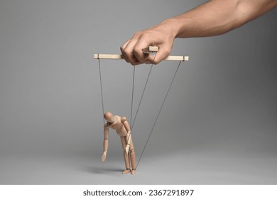Man pulling strings of puppet on gray background, closeup