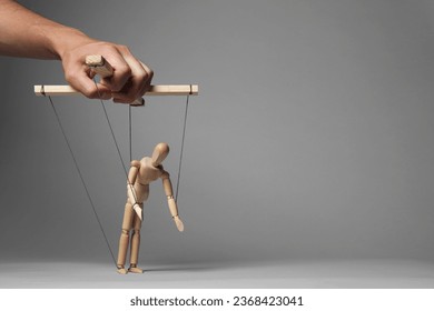 Man pulling strings of puppet on gray background, closeup. Space for text