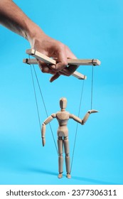 Man pulling strings of puppet on light blue background, closeup