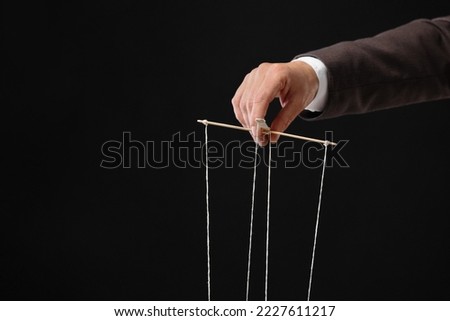 Man pulling strings of puppet on black background, closeup. Space for text