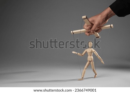 Man pulling strings of puppet on gray background, closeup. Space for text