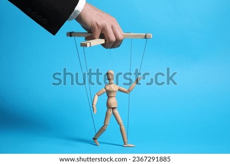 Man pulling strings of puppet on light blue background, closeup