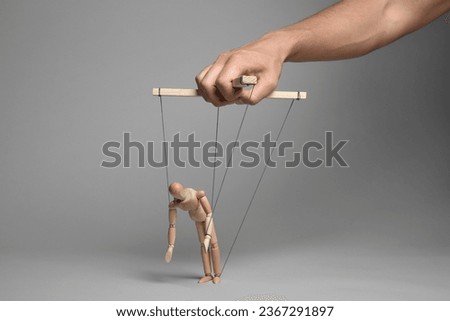 Man pulling strings of puppet on gray background, closeup
