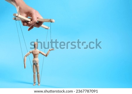 Man pulling strings of puppet on light blue background, closeup. Space for text