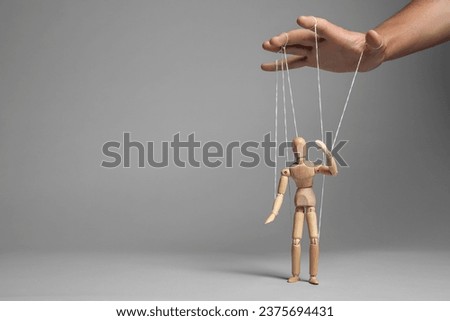Man pulling strings of puppet on gray background, closeup. Space for text