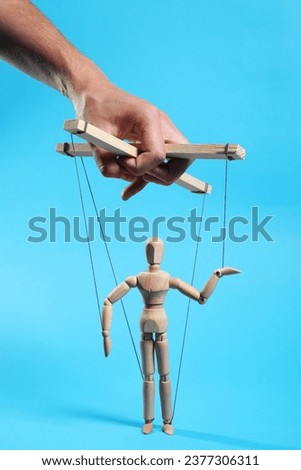 Man pulling strings of puppet on light blue background, closeup