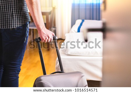 Man pulling suitcase and entering hotel room. Traveler going in to room or walking inside motel with luggage. Travel and holiday apartment rental concept.