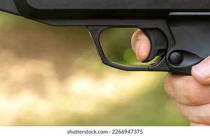 Man pulling the trigger of an air gun airgun, firing a pneumatic weapon, finger on the trigger side view, object detail, extreme closeup, one person shooting a pistol, about to shoot. Gun laws concept