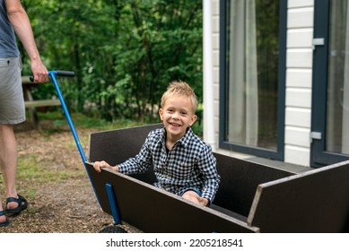 A Man Pulling A Wooden Wagon With His Son.