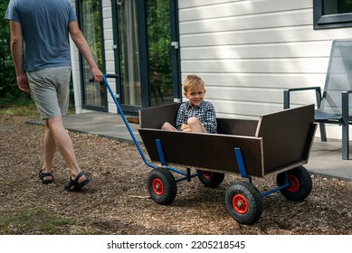 A Man Pulling A Wooden Wagon With His Son.