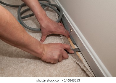 A man pulls back carpet in order to install insulation under the molding.