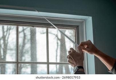 man pulls off tape backing as he prepares to insulate a window with plastic for winter heating season