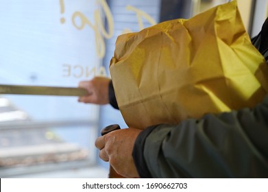 Man Pushes The Door Handle To Exit The Restaurant After Picking Up A Food Order (focus On Edge Of Paper Bag)