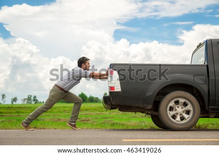 Man pushing a broken car down the road