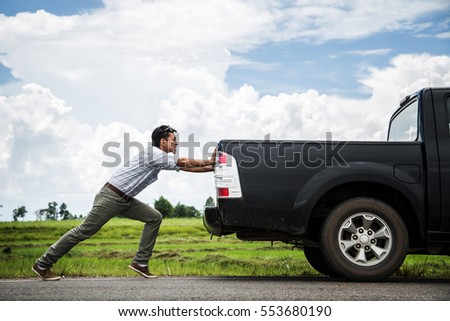 Man pushing a broken car down the road