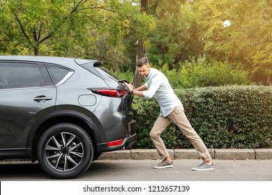 Man Pushing Broken Car On Road Along City Street