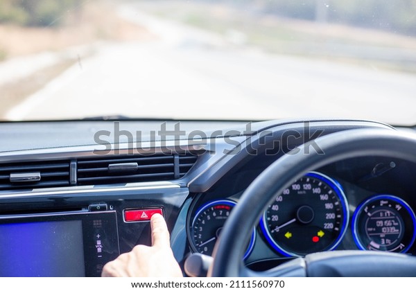 Man pushing a car hazard warning\
button red triangle, hazard lights, in an emergency\
situation.