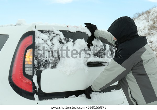 Man pushing car\
stuck in snow on winter\
road