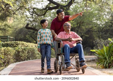 Man pushing old father on wheelchair while admiring view with son at park


