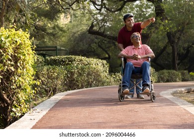 Man pushing old father on wheelchair having fun at park
