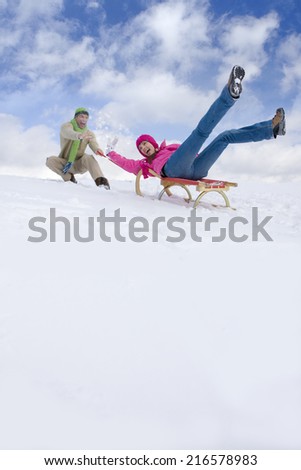 Man pushing woman down ski slope on sled