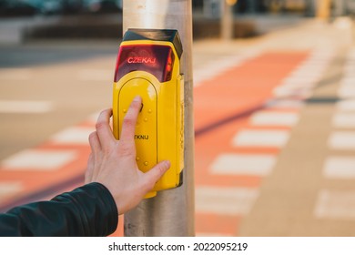 Man pushing the yellow button at a traffic light for pedestrians on the background of the road. Czekaj dotknij crosswalk button. Security. Poland. Polish. Safety