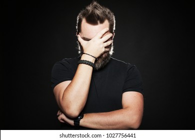 The man put his hand to his face in Studio on a black background. He's very unhappy and sad. Body language. Facepalm.