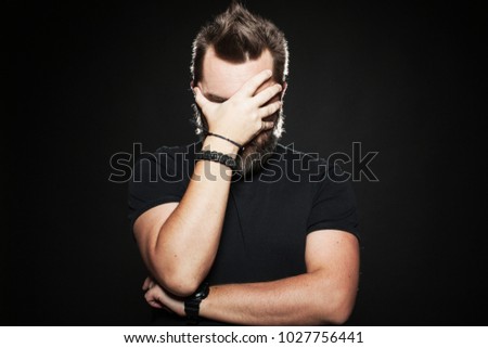 The man put his hand to his face in Studio on a black background. He's very unhappy and sad. Body language. Facepalm.