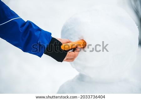 Man puts a carrot the a snowman figure, bodypart hand and arm, snowy background