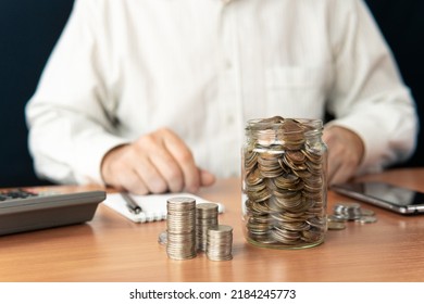 The Man Puts Down The Money Counts. Coins In A Glass Jar. Capital Accumulation.