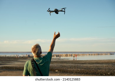 A man puts a drone on the arm of a drone descending after aerial photography of the area. In the background is a pond with tourists.                               
